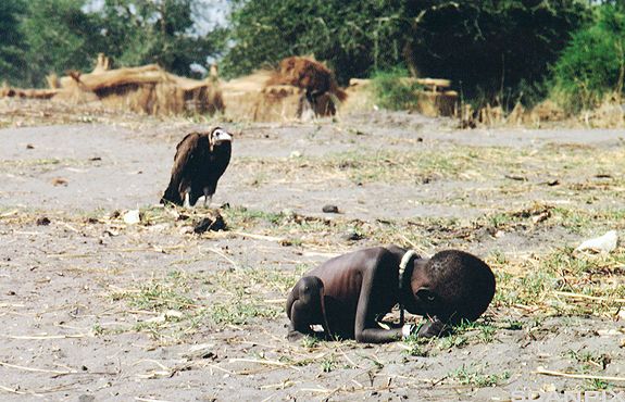Eit utmagra barn i Sudan ved sida av ein gribb. Foto. 