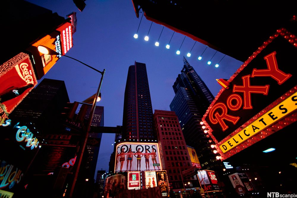 Mange neonlys i by med skyskraparar og andre høge bygg som står tett inntil kvarandre. Foto.