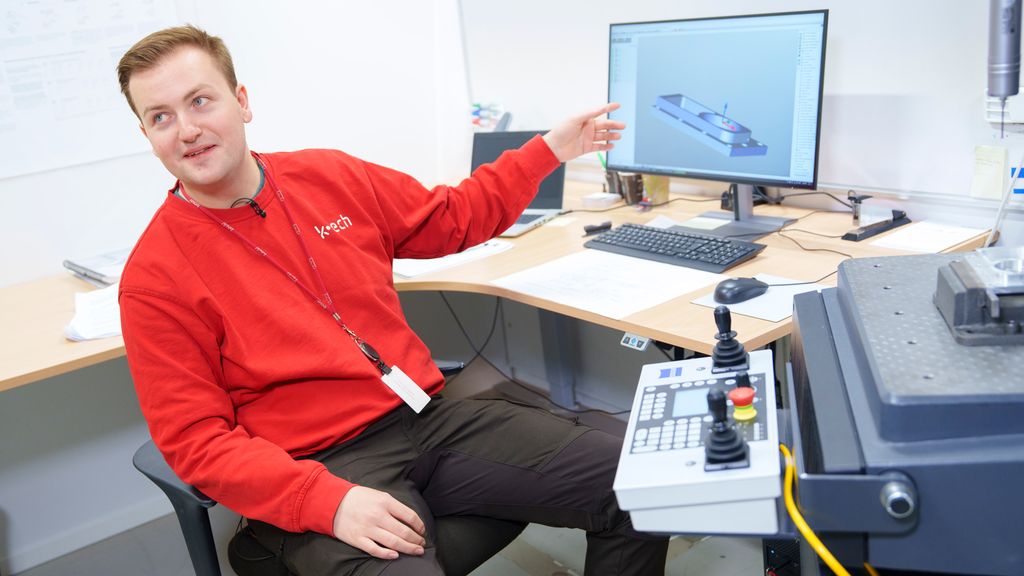 Person som sitter ved et bord og peker på en dataskjerm. Foto.