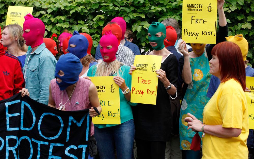 Demonstrantar i fargerike finlandshetter held plakatar med logoen til Amnesty International og bodskapen "Free Pussy Riot!" på. Foto. 