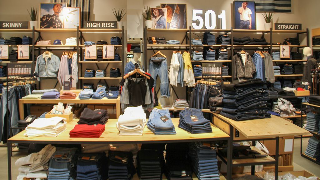 Butikkinteriør frå ein klesbutikk. Plagga er ordna på bord, hyller og stativ med kleshengarar. Foto.