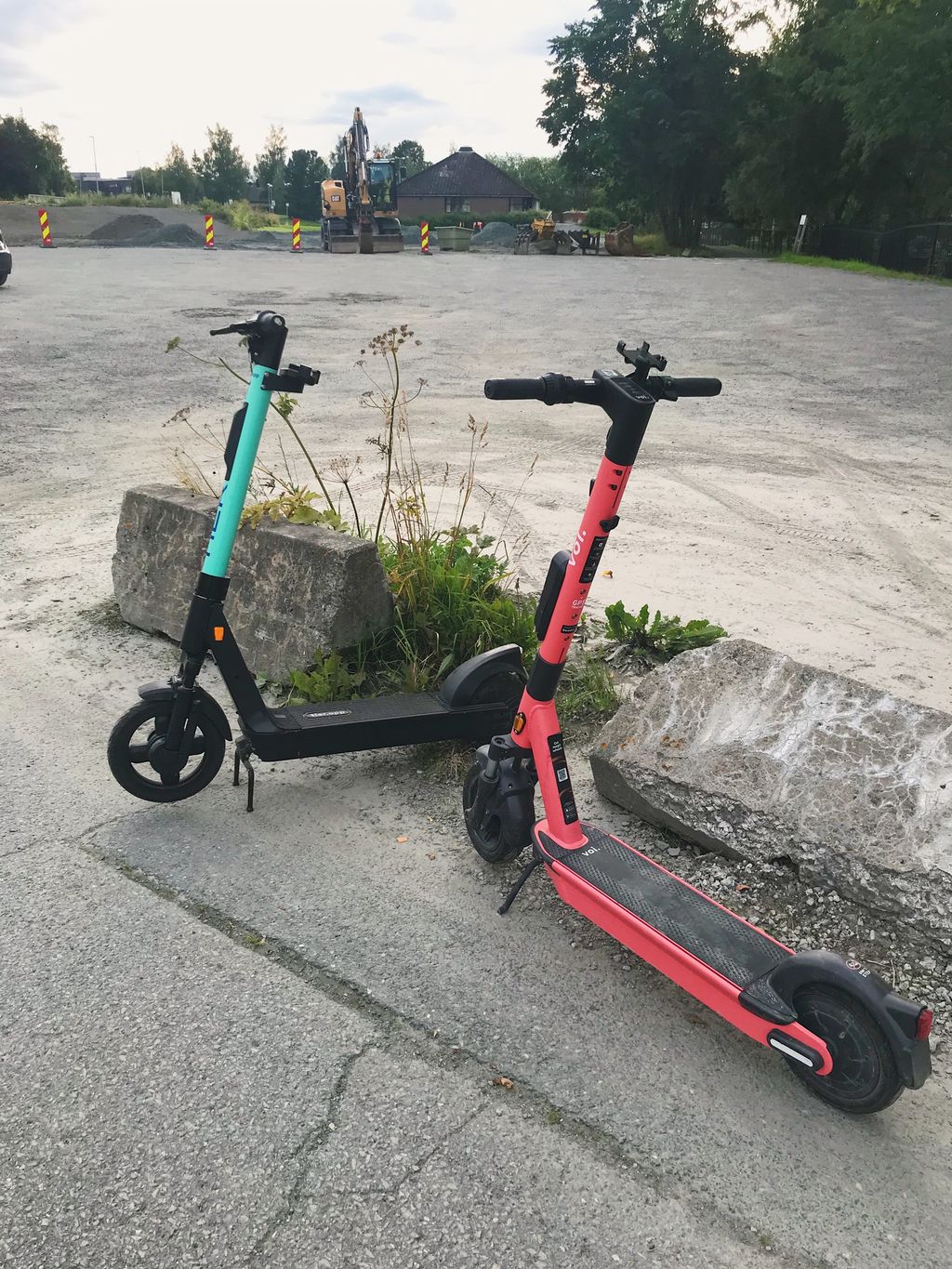 To sparkesykler som kan leies ut, en rød og en grønn, står på fortauet foran en betongkant. Foto.