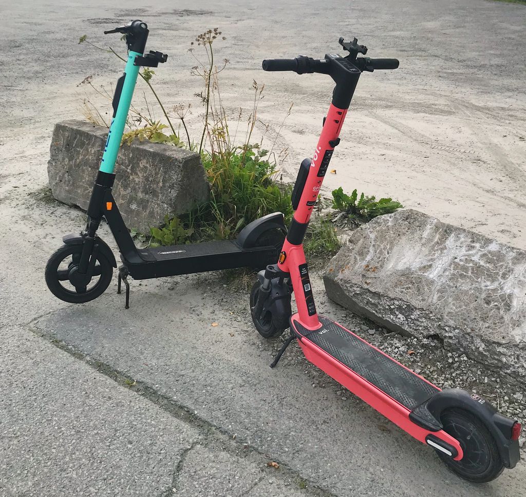 To sparkesykler står på fortauet foran en betongkant. Den ene sykkelen er rød, den andre grønn. Foto.