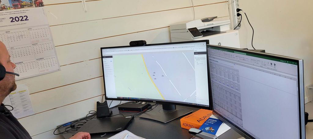 En mannlig befrakter i arbeid. Han sitter foran to dataskjermer. Den ene skjermen viser et kart, den andre et regneark. Foto.