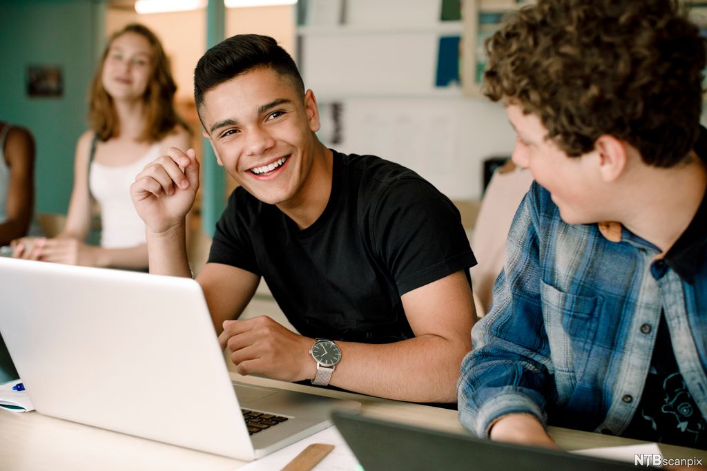 To gutter sitter og smiler foran en dataskjerm. Foto.