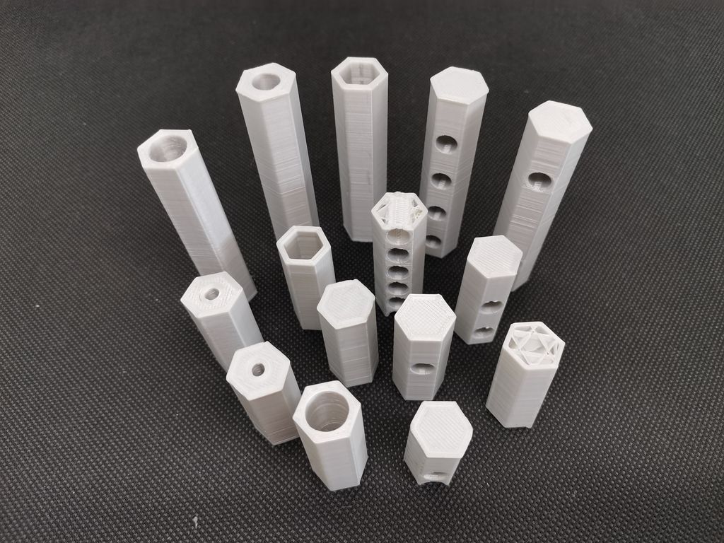 Femten hvite, sekskanta staver oppstilt på et bord. De er av ulik høyde og har hull av ulik størrelse både i sentrum og på sidene.