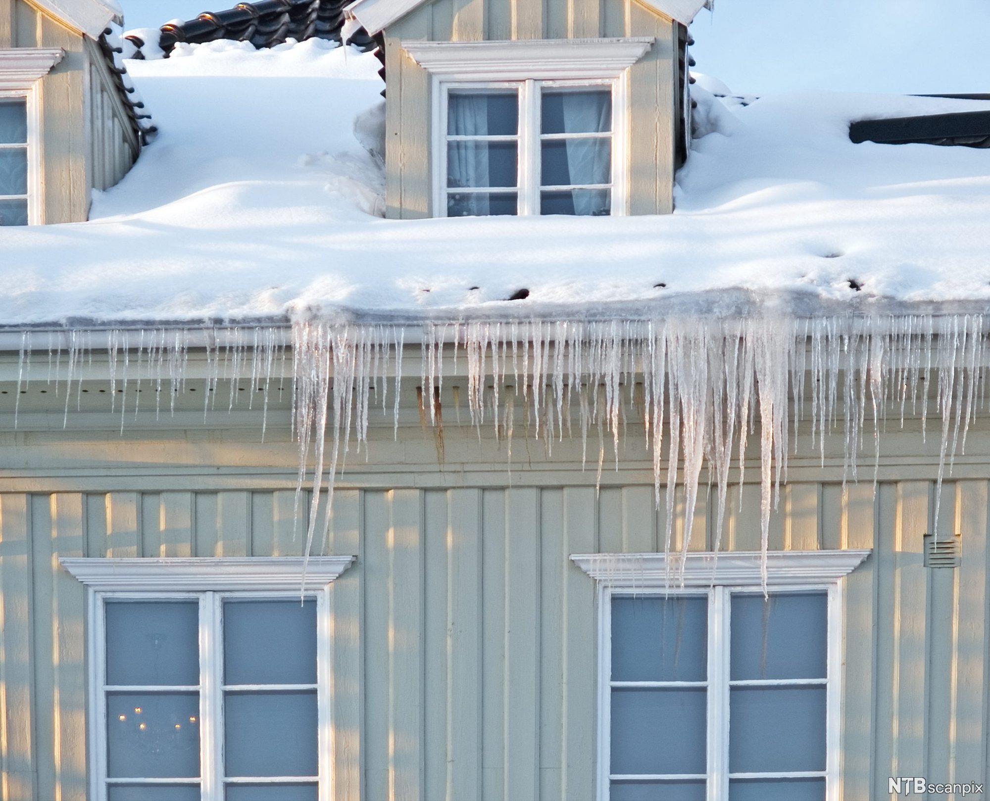 Istapper som henger ned fra en takrenne over to vinduer. Foto.