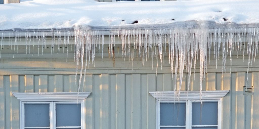 Istapper som henger ned fra en takrenne over to vinduer. Foto.