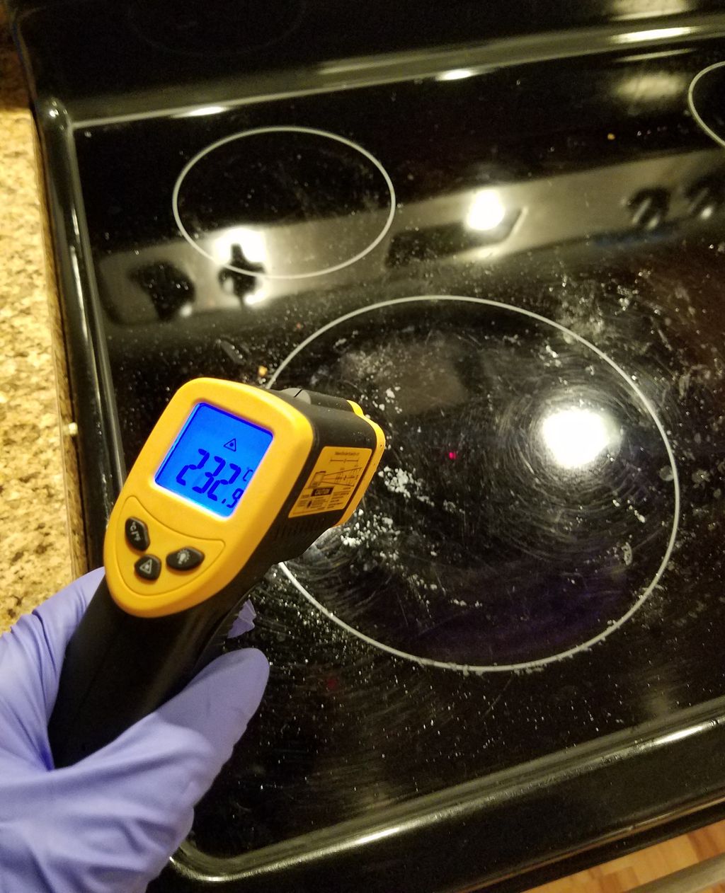 Hånd som holder et måleapparat som måler temperatur på ei kokeplate. Displayet viser 232,9 grader. Foto.