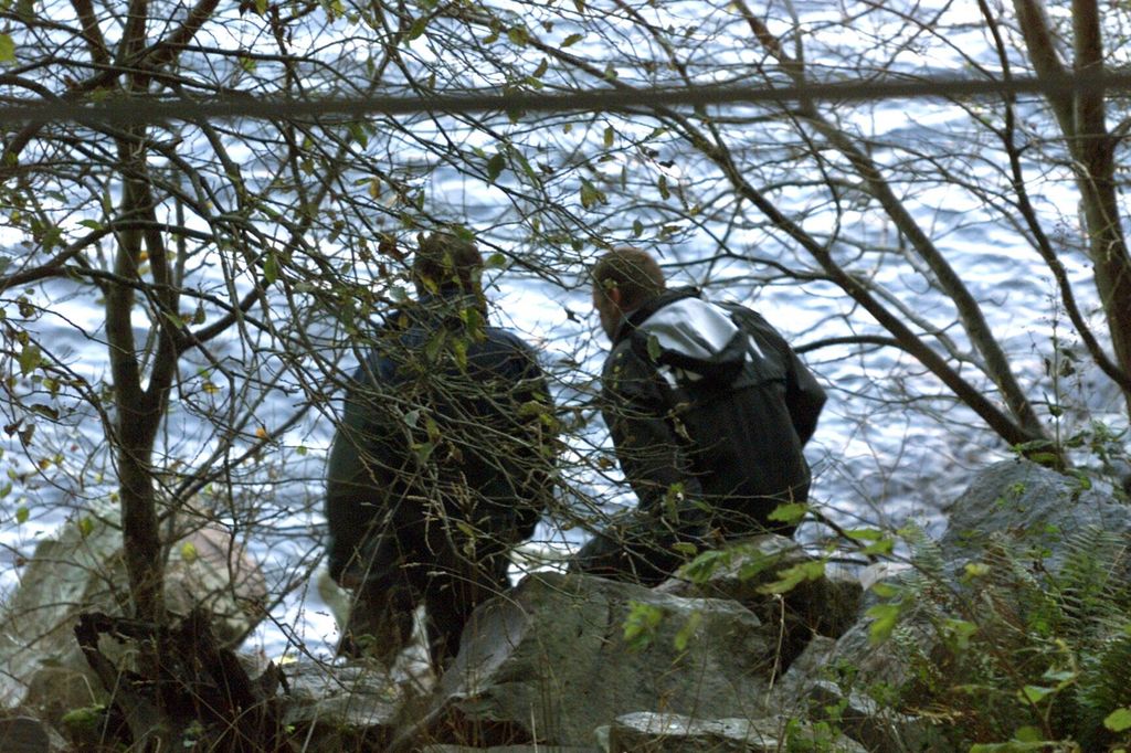 To personer i uniform undersøker noe i skogen. Foto.