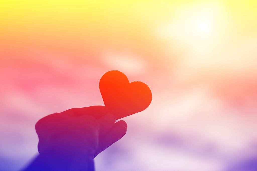 A hand holds up a heart, everything is rainbow coloured. Illustration.