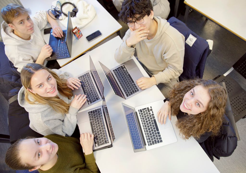 Fem elever sitter rundt et bord med hver sin pc. Foto. 