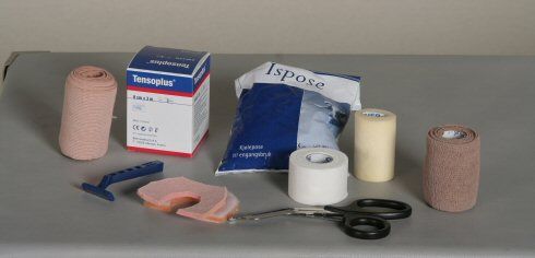 Bandasje, barberhøvel, saks, ispose og sportstape på et bord. Foto.