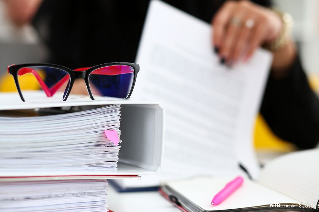 Bunke med ringpermer ligger på arbeidsbord. Foto.