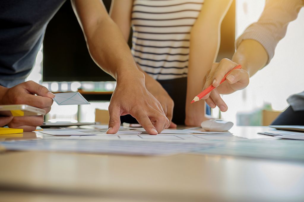 Nærbilde av hender, med og uten blyant, over et ark. Samarbeid om utvikling av merkevare. Foto.