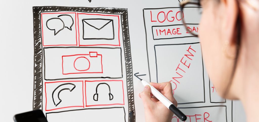 Person framom tavle teiknar ei skisse av ein app med ikon for chat, melding, foto, telefon og høyretelefonar. Foto.