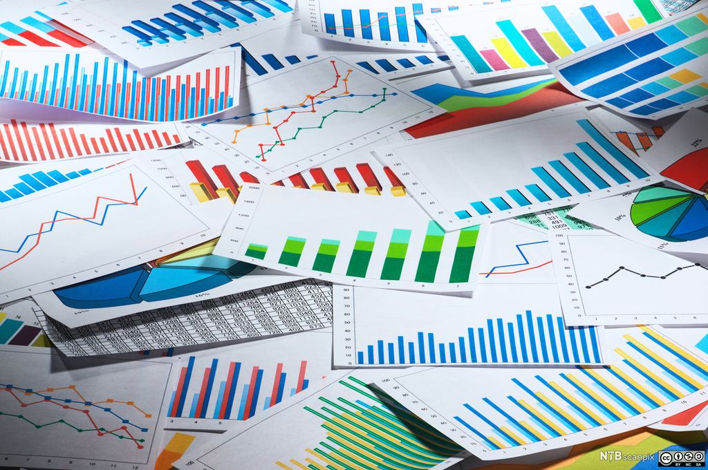 Utskrifter av diagrammer og grafer i ulike farger ligger spredt utover et bord. Foto.