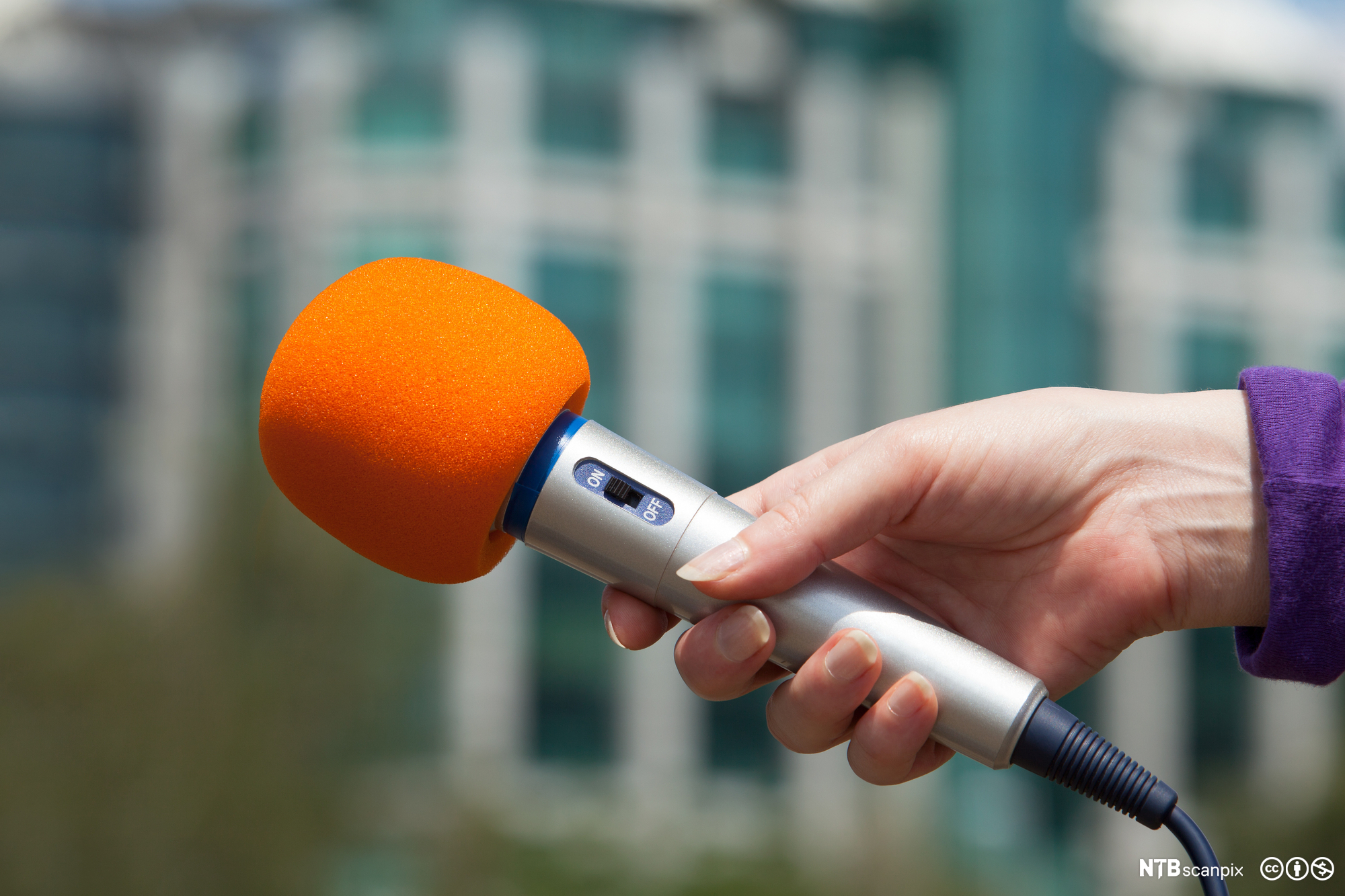 A hand holding an orange microphone. Photo.