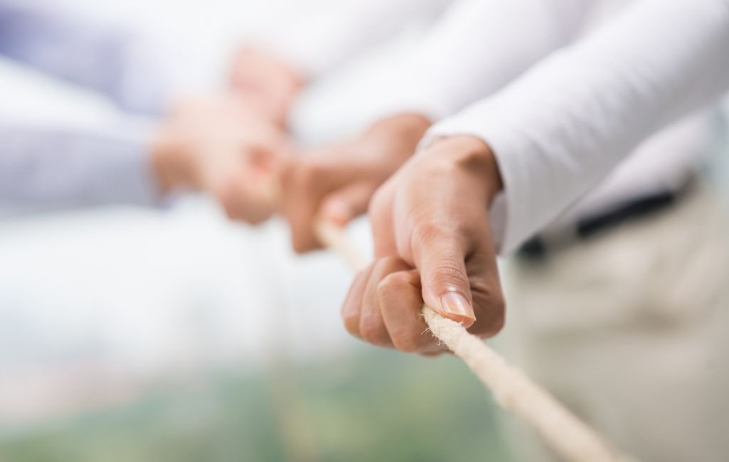 Flere hender trekker i et tau. Foto.