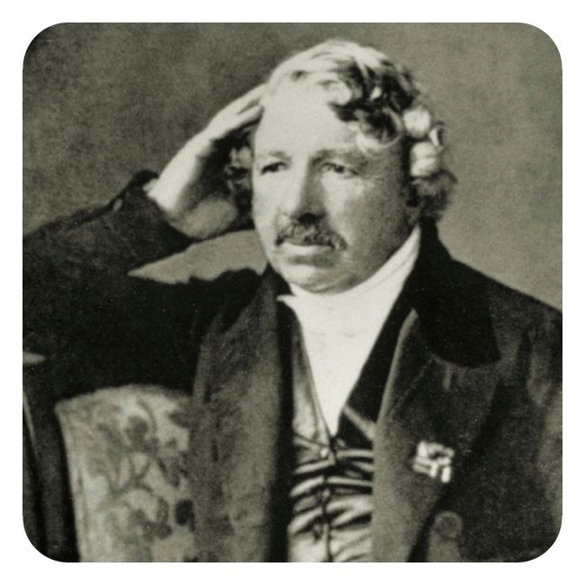 Svart-hvitt-fotografi som viser en mann på mellom førti og femti år. Han har relativt kort hår som faller i lokker, og en kraftig mustasje. Han sitter på en stol med ryggstø som han har lagt overarmen på, og han støtter hodet med handa. Han har på seg hvit skjorte, blank silkevest og dressjakke. 