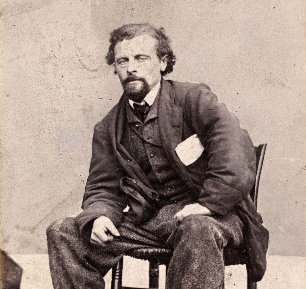 Portrett av Marcus Thrane ca. 1863. Han sit breibeint og litt framoverlent på ein stol. Han er uvørdent kledd, buksa er oppbretta og har lapp på kneet. Han har nokre papir i brystlomma. Foto.