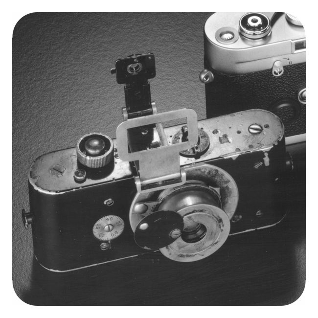 Svart-hvitt-fotografi som viser et velbrukt handkamera av typen Leica. Kameraet er avlangt og nokså smalt, med en klaff foran linsa. Kamerakroppen er svart, men linsa og enkelte andre deler er sølvfarga.  