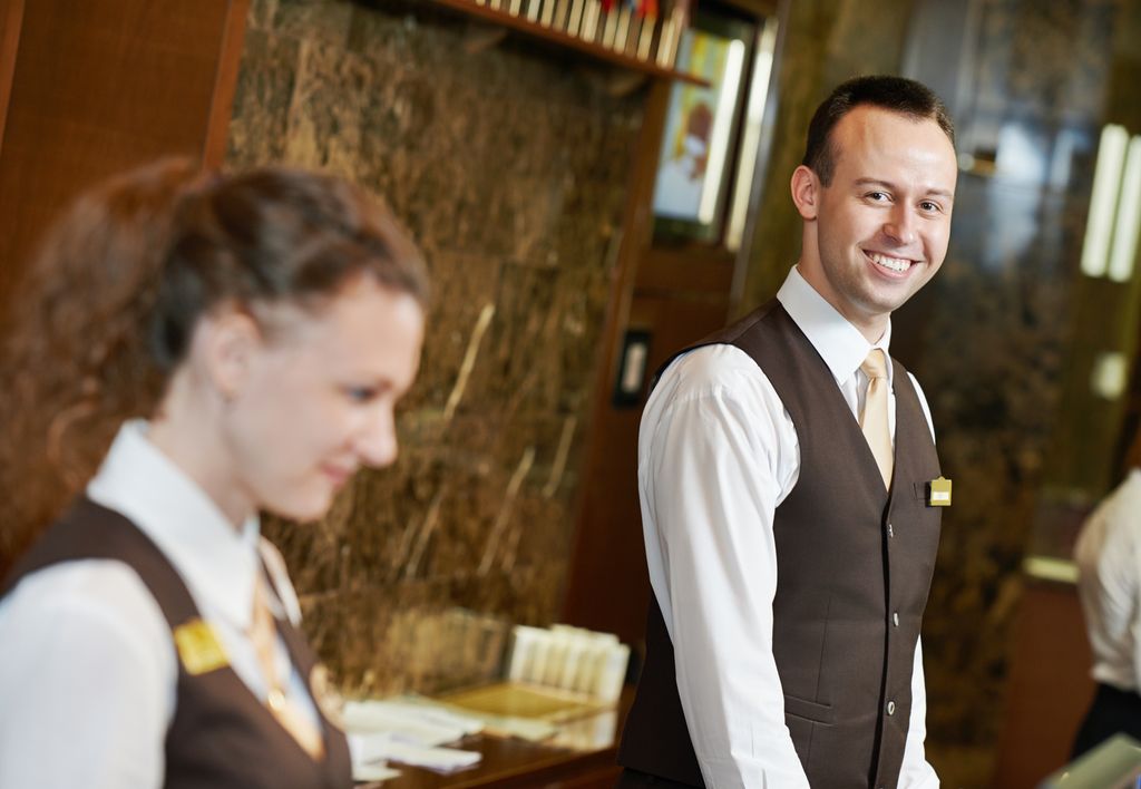 Foto av glad resepsjonist som står ved disken.