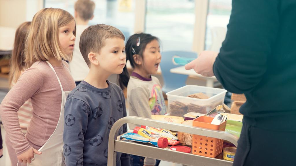 To jenter og en gutt står i kø foran matserveringen på SFO. Foto.