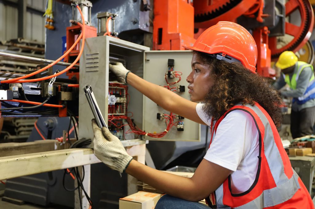 En ung arbeider betjener eller reparerer elektriske fordelingstavler til metallmaskinverktøyet i fabrikk- eller maskinindustrien. Foto.