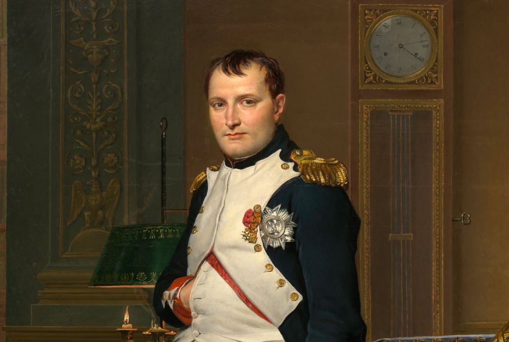 Napoleon i uniform i sitt kontor. Han ser mot betrakteren og har hånden karakteristisk stukket inn i jakken foran. Jakken er utstyrt med medaljer og gull på skuldrene. Maleri.