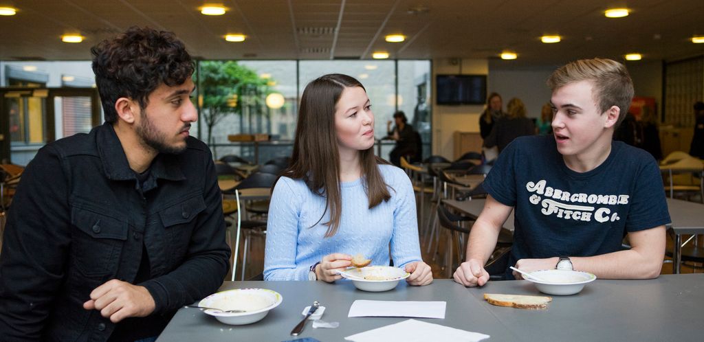 Tre elever spiser og snakker sammen i kantina på en videregående skole. Foto.