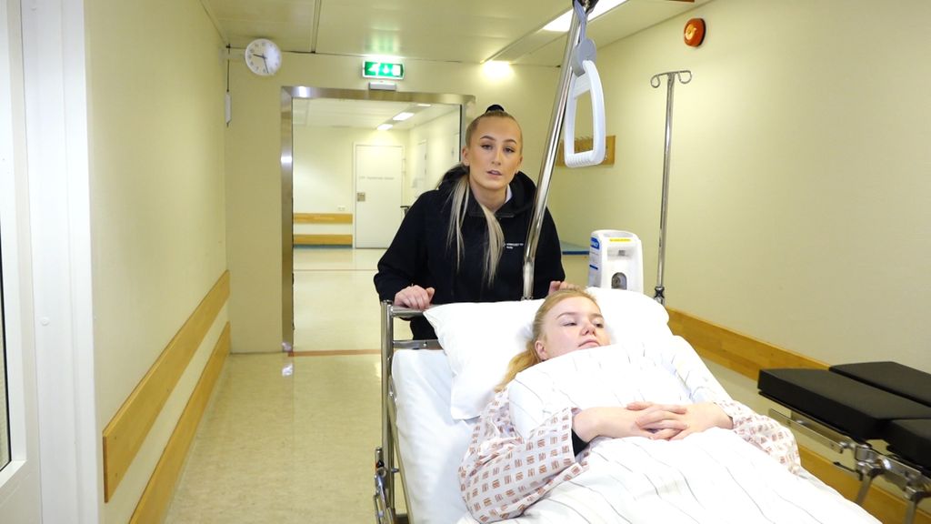 En portør transporterer en pasient som ligger i ei seng. Foto.