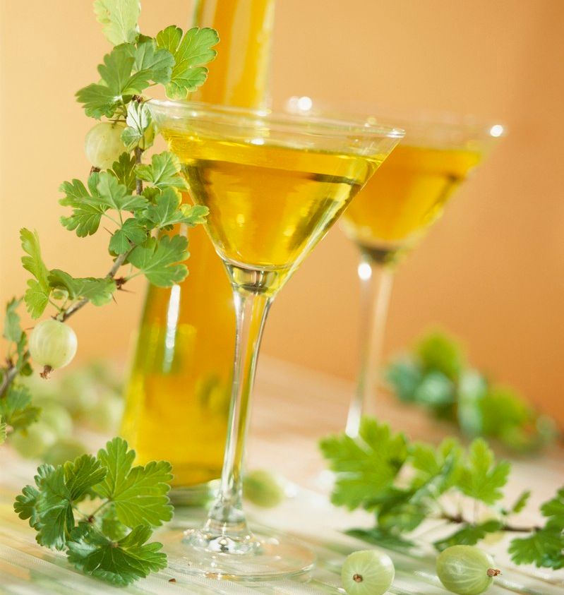 To stettglass med et gult, halvveis gjennomsiktig innhold på et bord. Rundt glassene ligger det grønne bær og grønne blader. Foto.