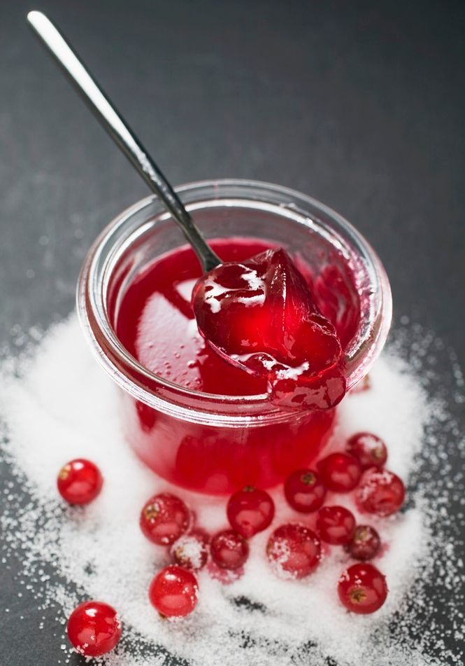 Ripsgelé i et glass. Utenfor glasset er det strødd sukker blant flere hele ripsbær. Foto.