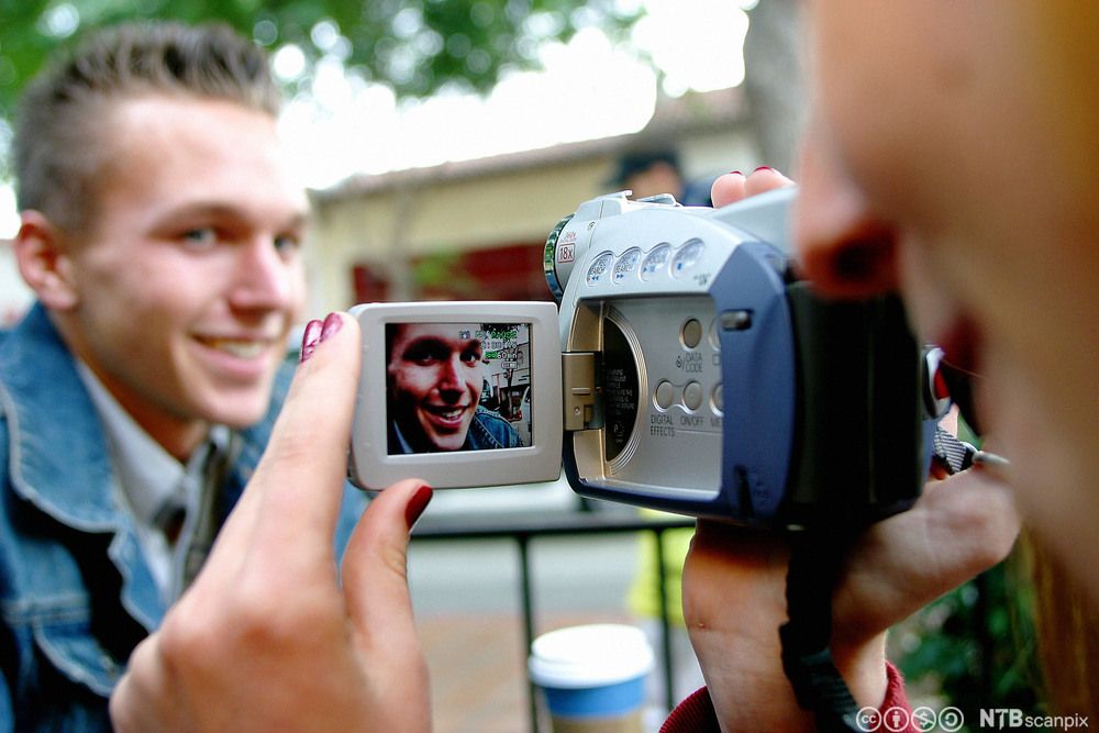 Nærbilete av eit videokamera som filmar ung mann. Foto.