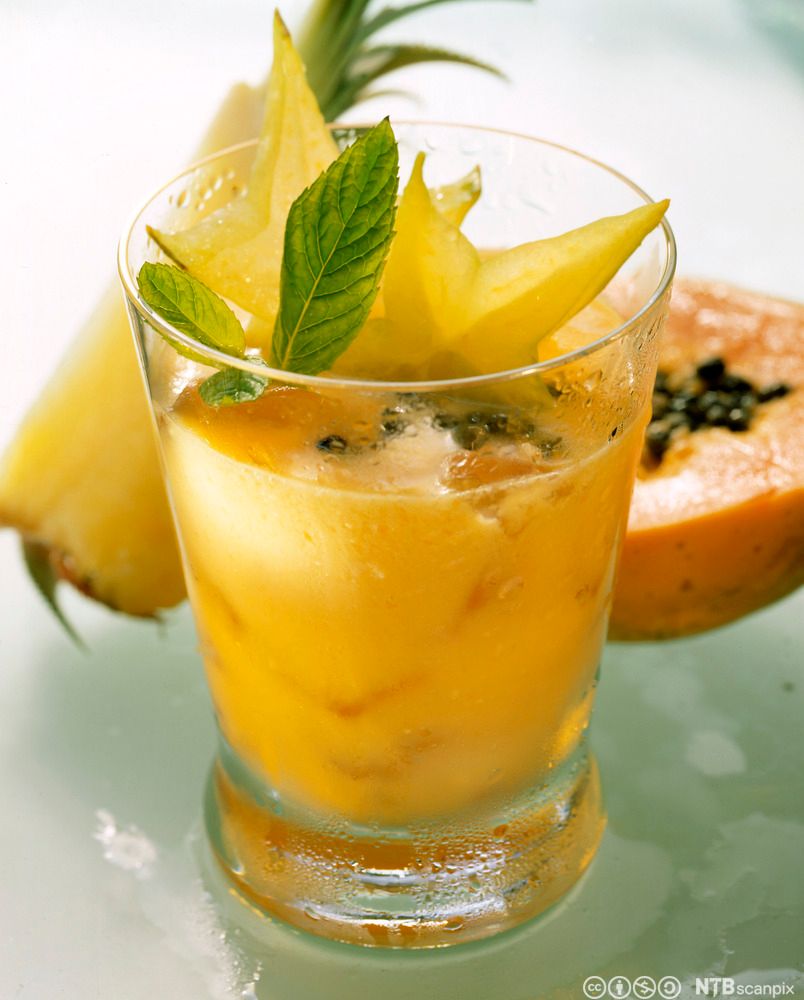 Ein gul drink i eit glass, pynta med carambola og mynte. Foto.