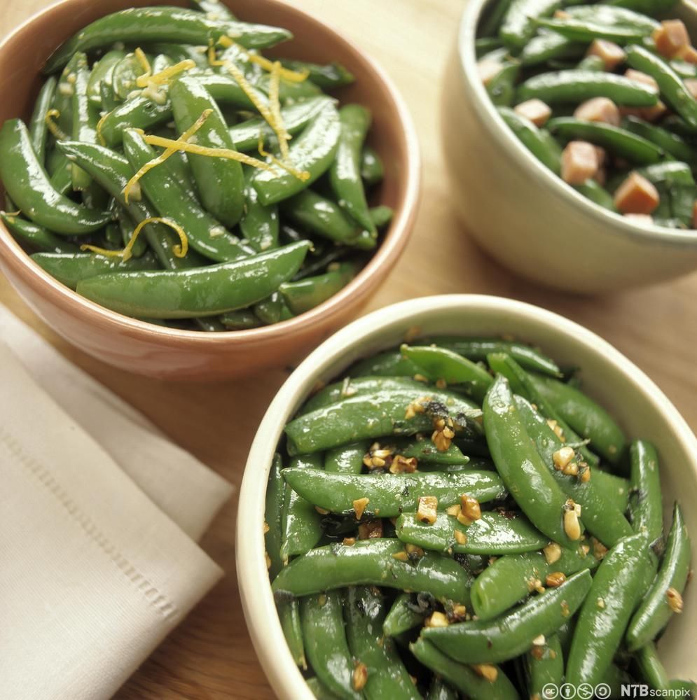 Tre skåler med grønne sukkererter med ulik garnityr. Foto.