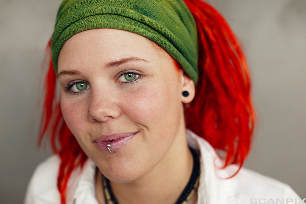 Jente med rødt hår, grønne øyne og piercing i leppa. Foto.