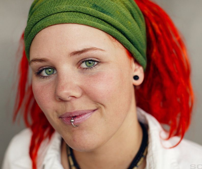 Jente med rødt hår, grønne øyne og piercing i leppa. Foto.
