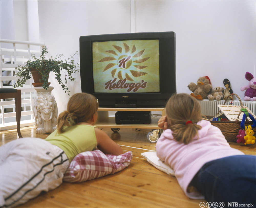 To jenter ligger på gulvet og ser på TV. Foto.