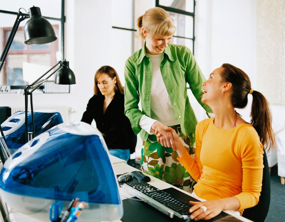 To kvinner hilser på hverandre på et kontor. De smiler og har øyekontakt. Foto.