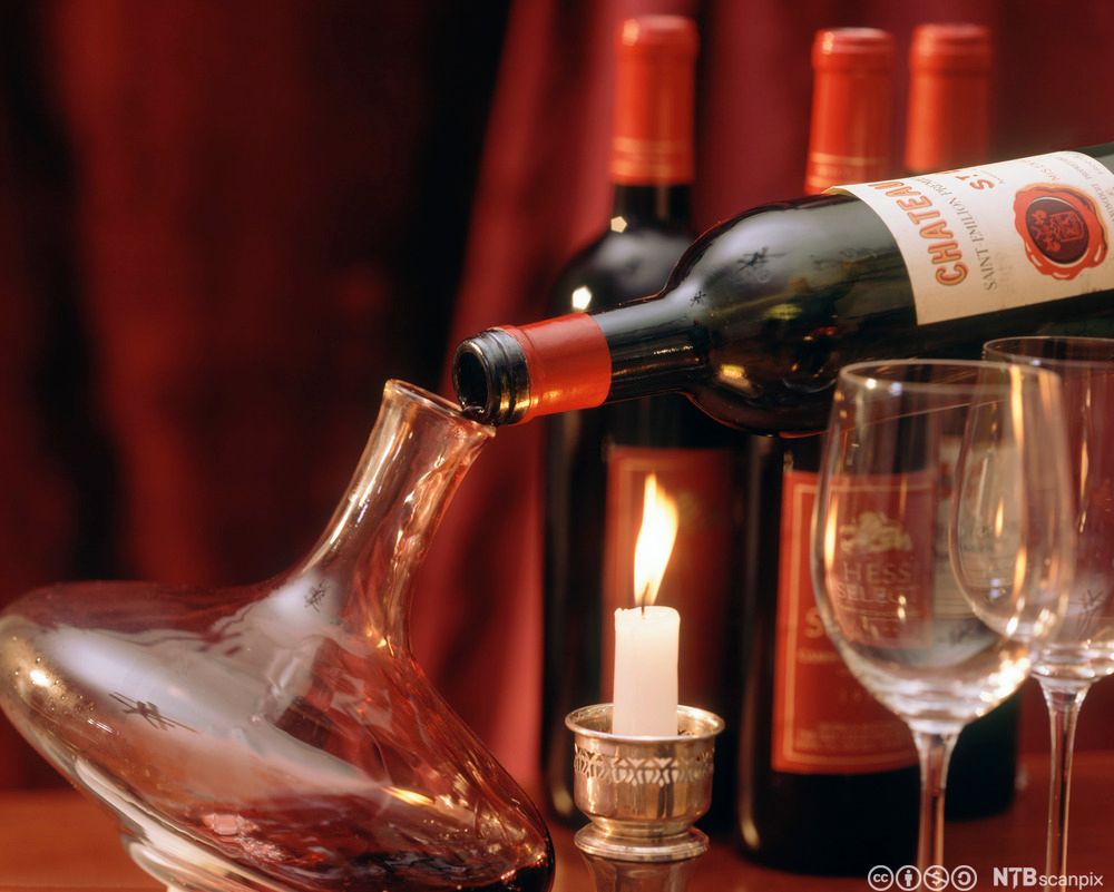 Vinflaske som dekanteres ved å helles forsiktig over i en karaffel. Foto.