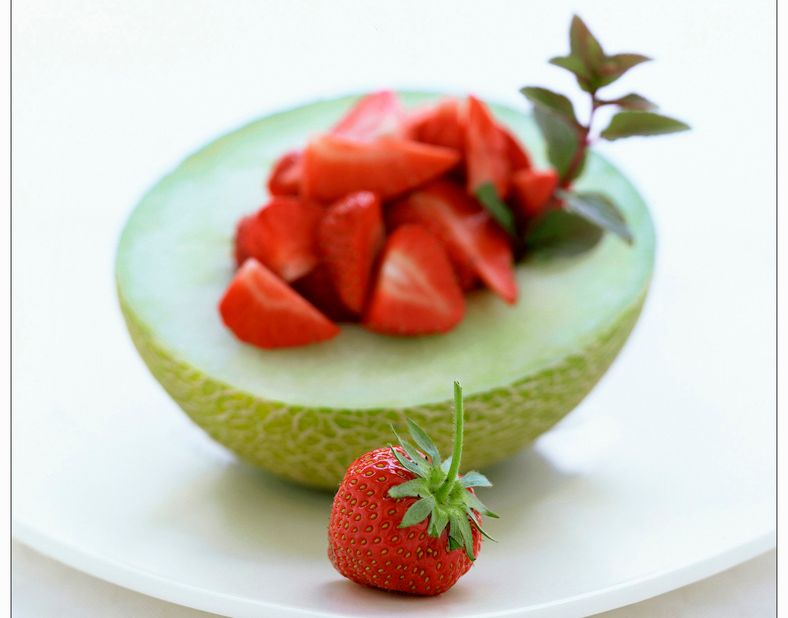 Halv grøn melon lagt til på eit kvitt fat. Frøa i kjernen er fjerna og erstatta med oppskorne jordbær. Foto.