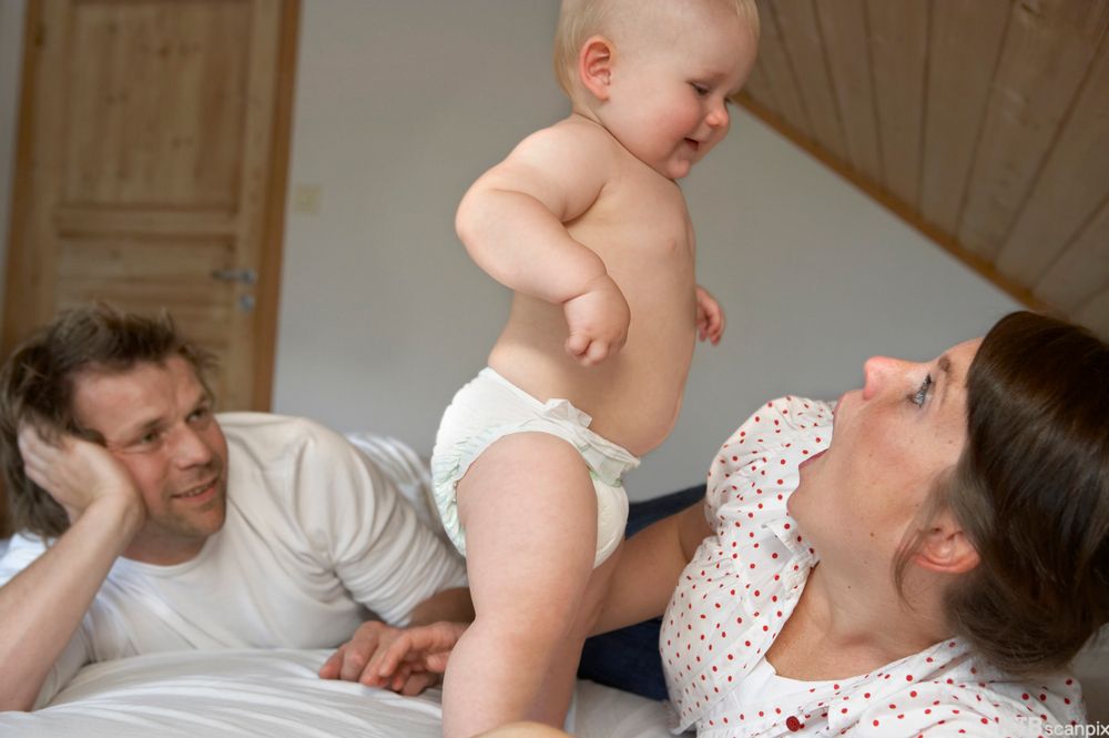 Kjernefamile med mor, far og barn i ei seng. Foto.