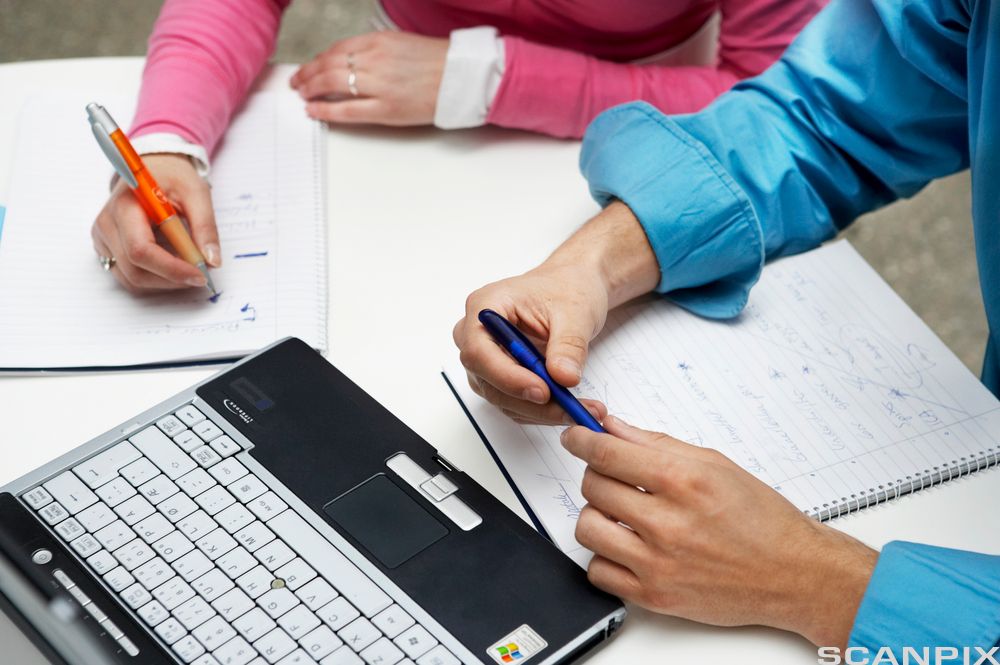 Hender på notatblokk ved en pc. Foto.