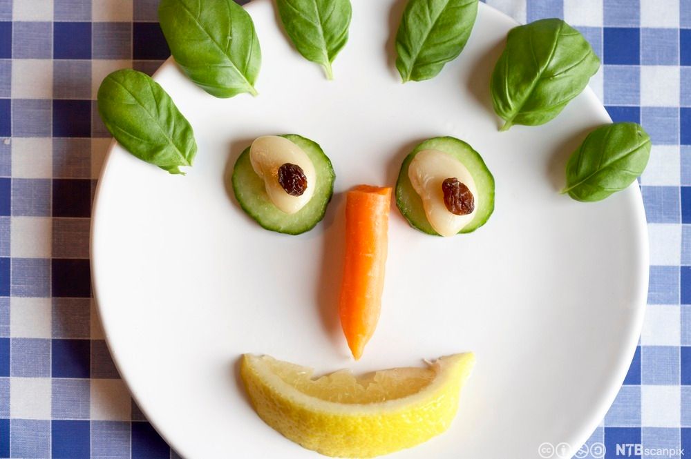 Ansikt laget av grønnsaker på en hvit tallerken. Foto.