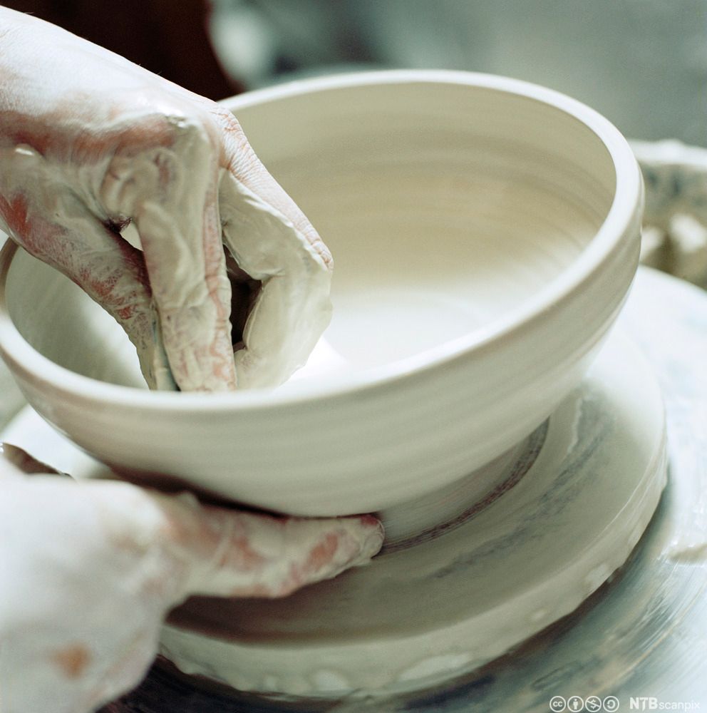 Hender som jobber med ei skål i  leire. Foto.