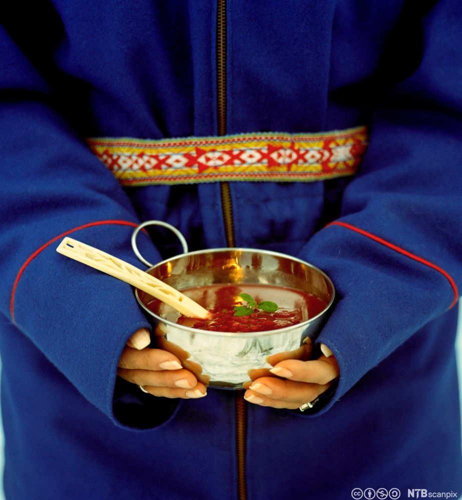 Kvinne i samedrakt holder suppeskål. Foto.