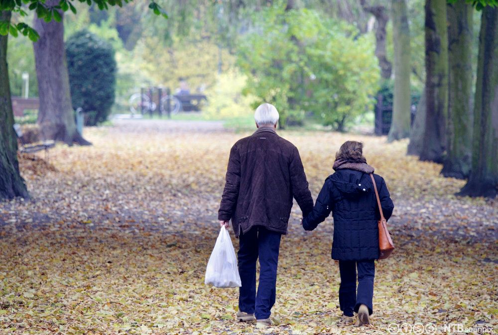 Eldre par går tur gjennom høstløv i en park. Foto.
