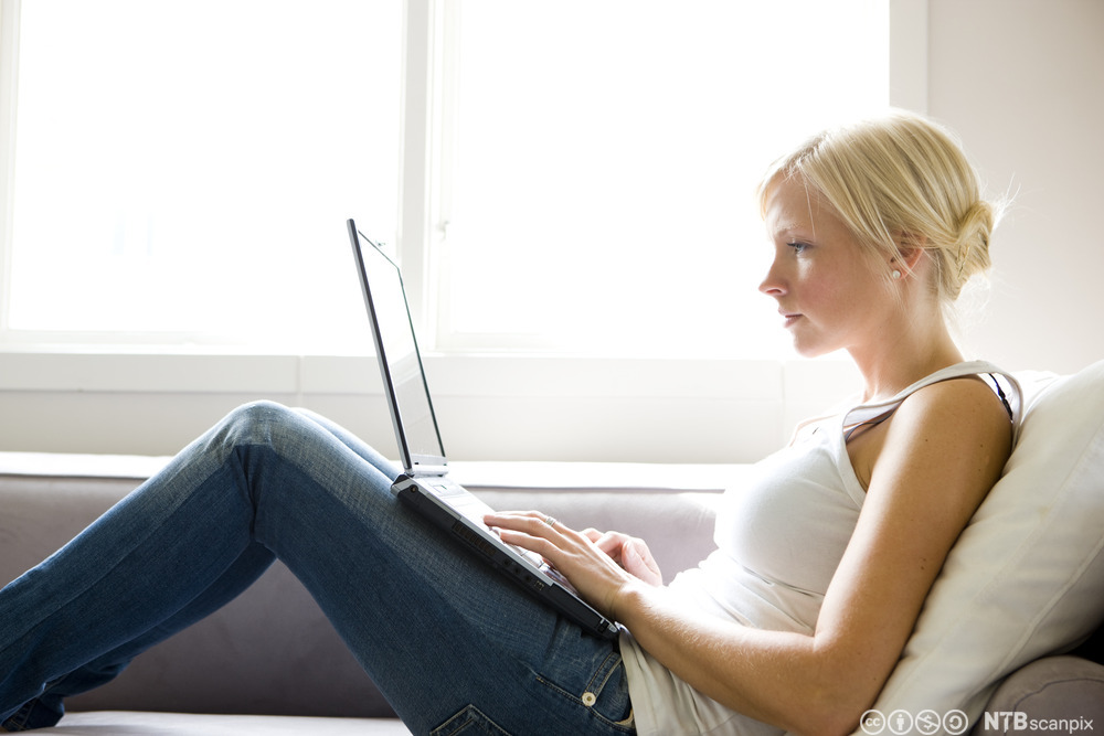 Ung kvinne med bærbar datamaskin i fanget. Foto.